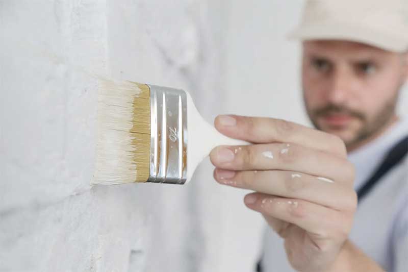 Painting a white brick wall with a paint brush